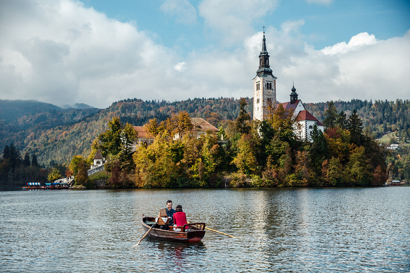 Moški in ženska veslata v ladjici na blejskem jezeru s pogledom na otoček s cerkvijo