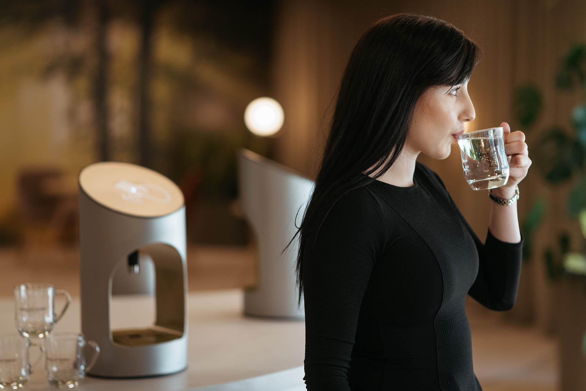 Črnolasa ženska v črnih oblačilih s kozarcem v roki pije vodo