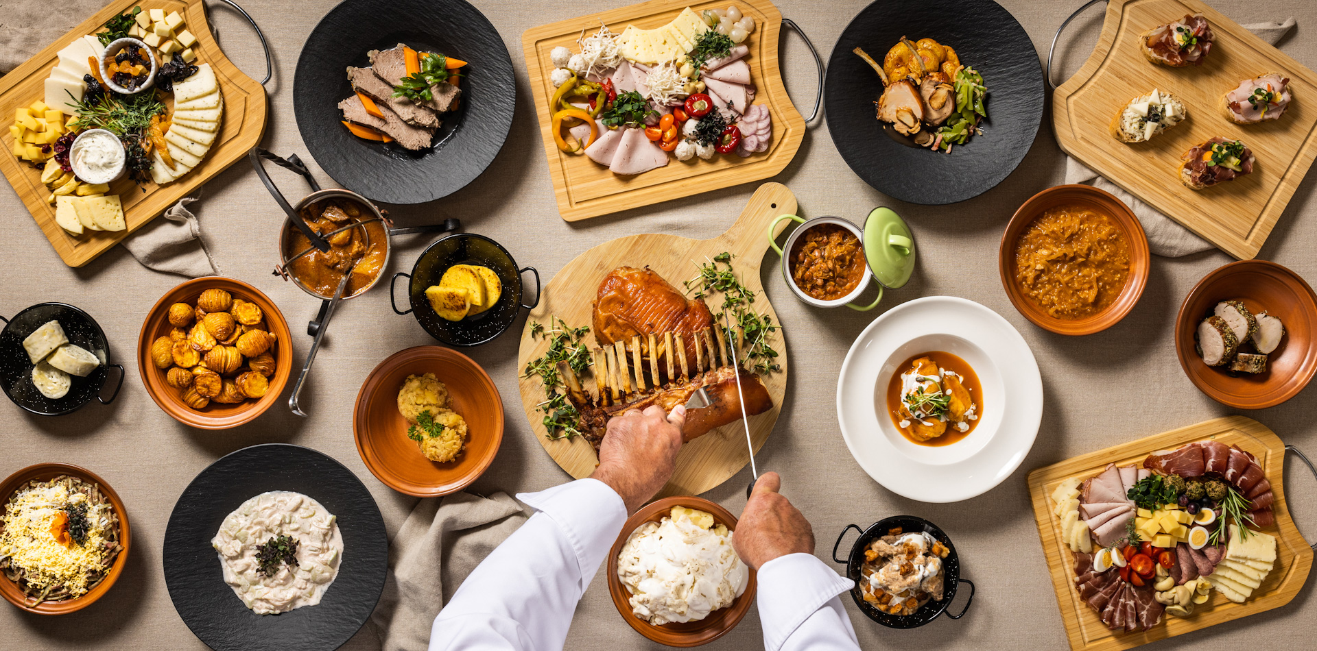 Polna miza tradicionalnih prekmurskih dobrot in kuhar, ki na pladnju reže pečenko