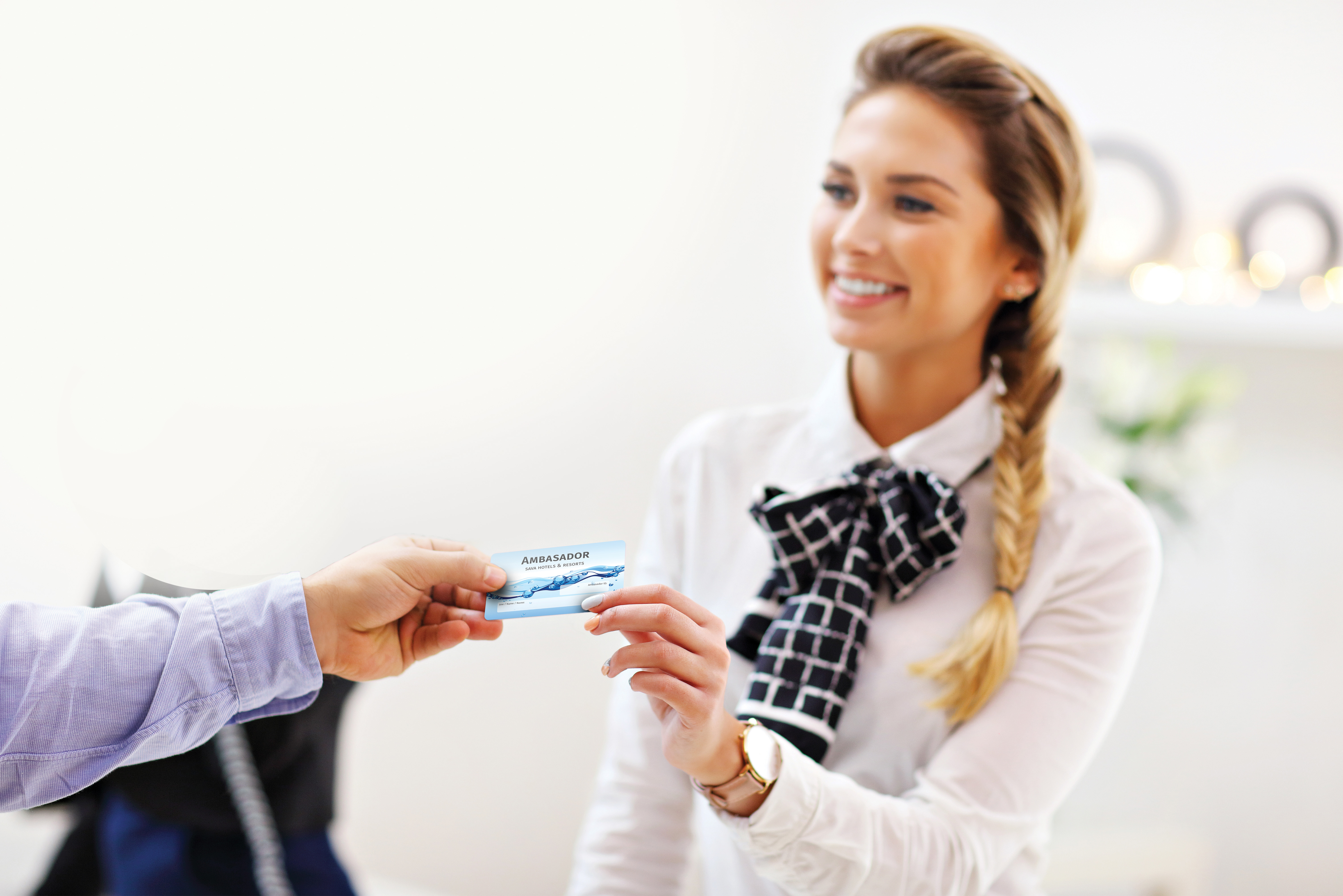 Ženska v beli srajci drži v roki kartico z napisom "ambasador" in jo daje v roke gostu