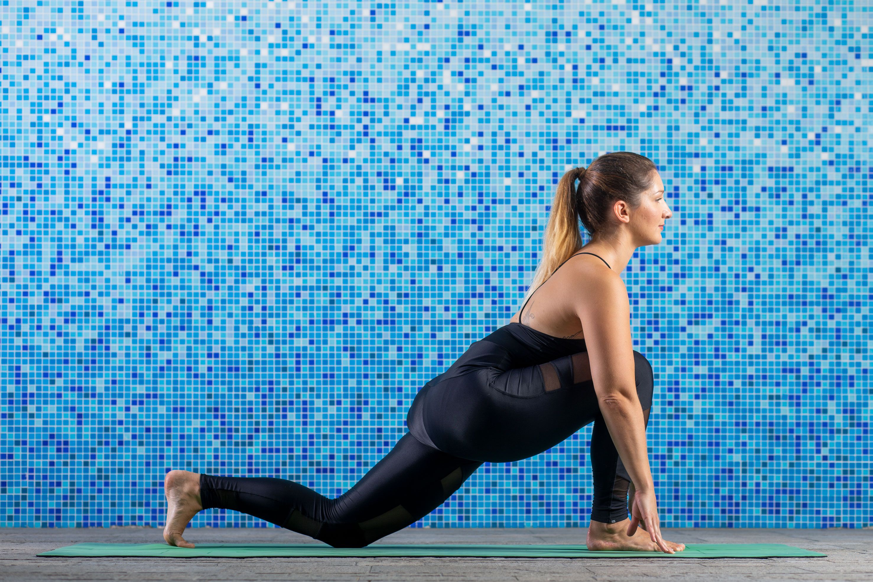 Ženska v črnih športnih oblačilih v položaju "izpadni korak" izvaja jogo