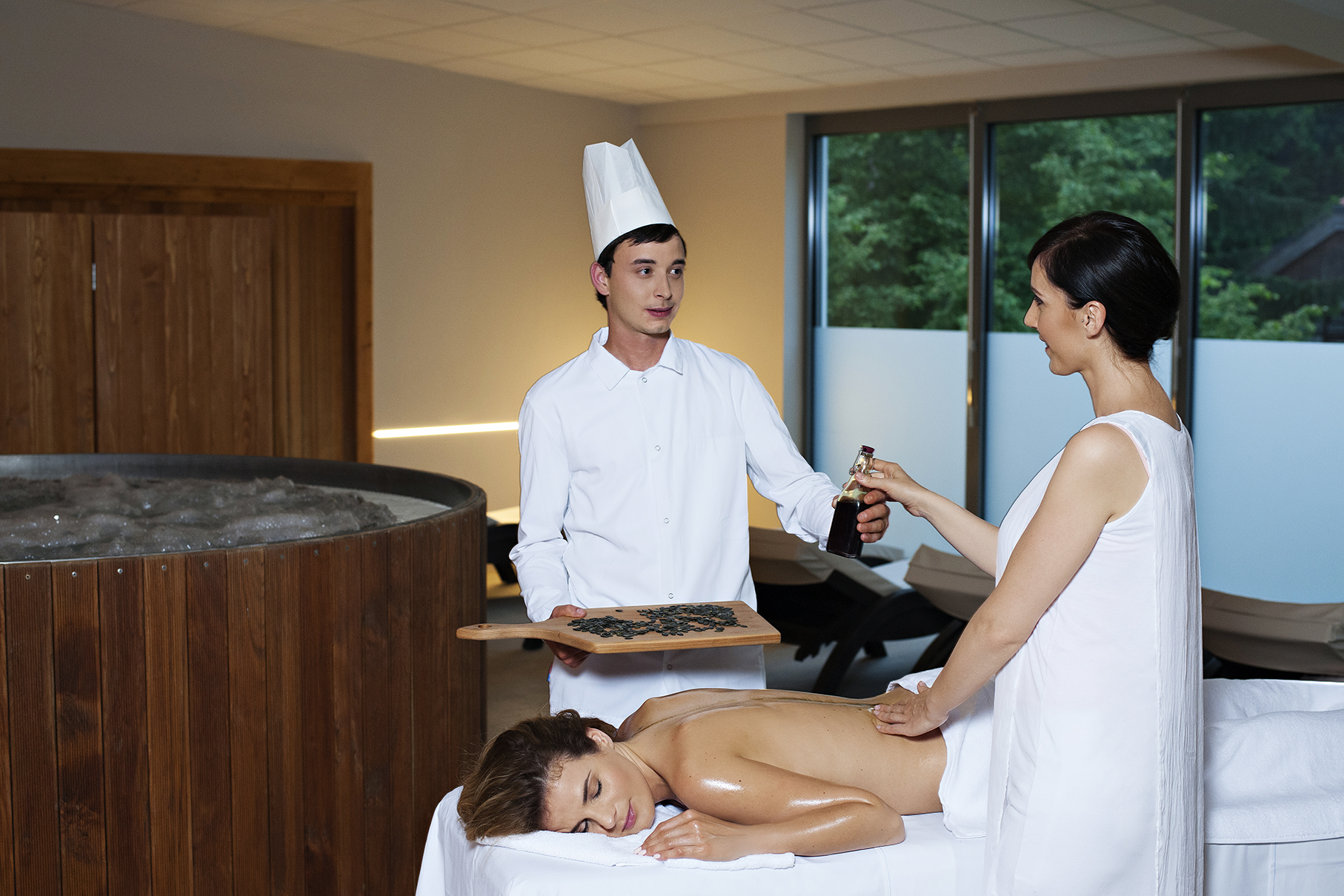 Kuhar je prinesel bučno olje maserki, ki masira žensko na masažni mizi