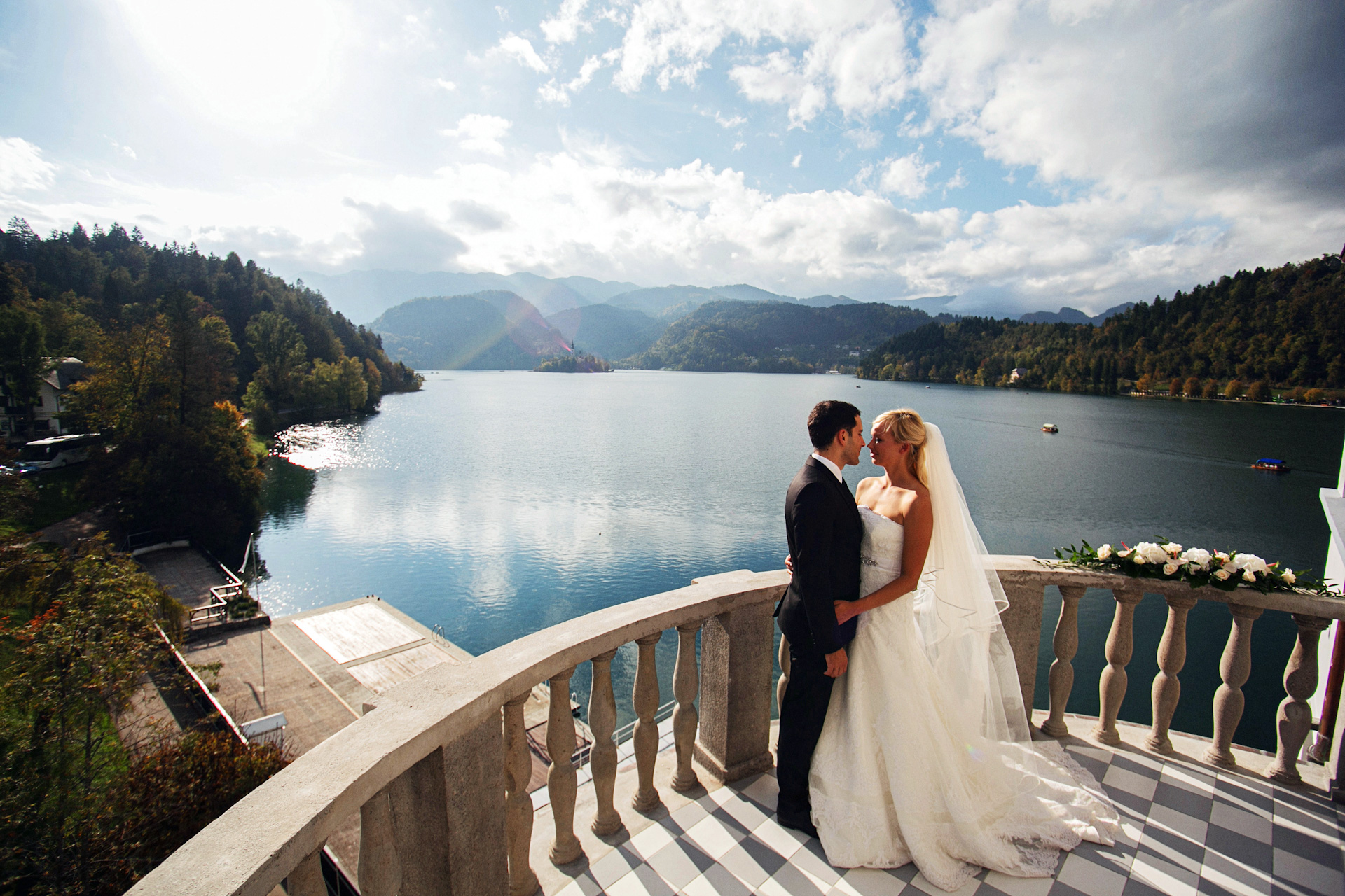 Ženin in nevesta se objemata in stojita na terasi s pogledom na blejsko jezero