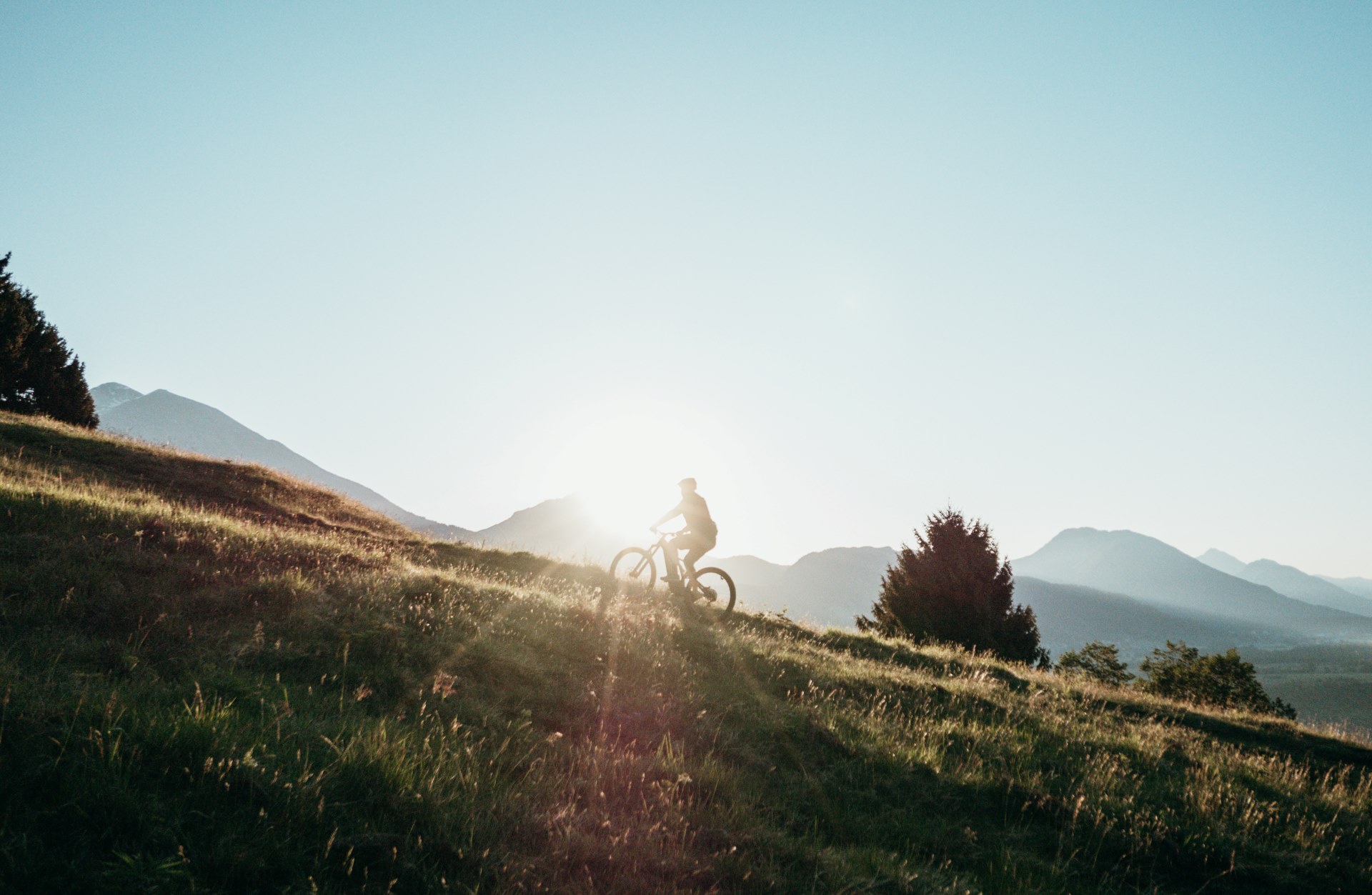 Cyclist riding a mountain trail at sunset with mountain views.