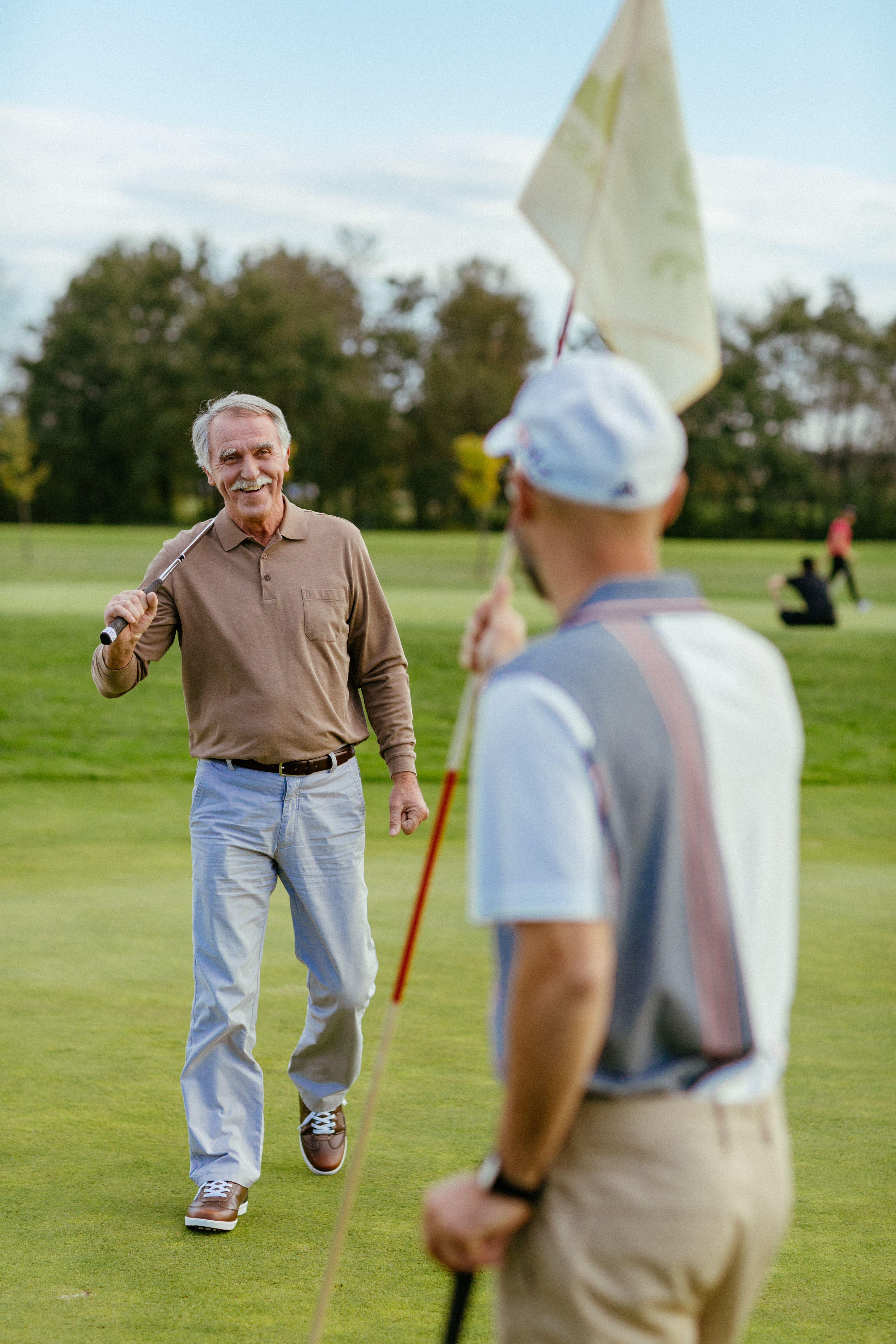 Moški v športnih oblačilih z golf palico v roki se pogovarja z drugim moškim na golf igrišču